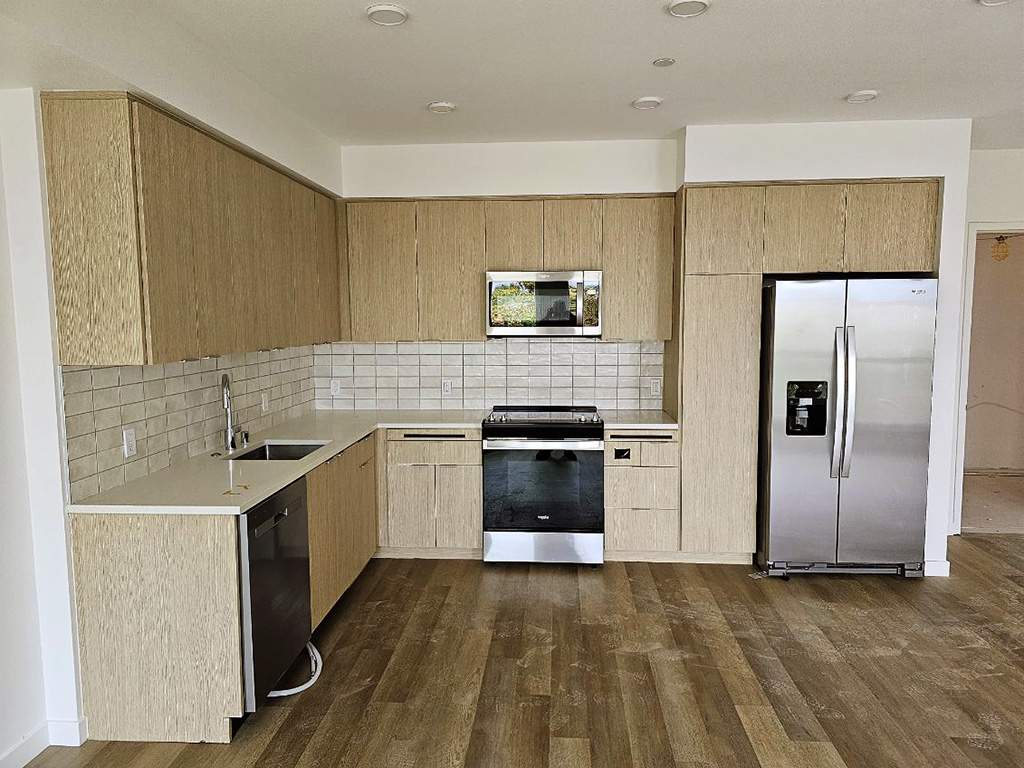 New kitchen in a small apartment, tan wood cabinets and drawers, no island, L shaped with dishwasher on the left and oven on the right.