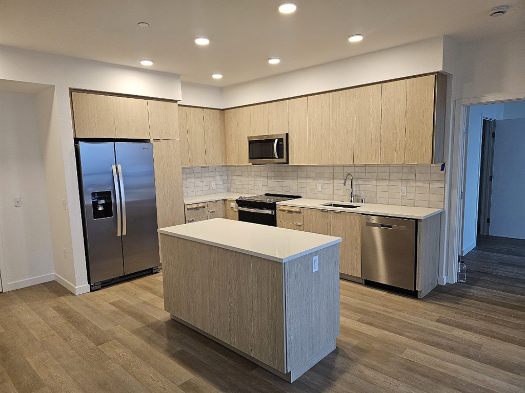 New kitchen in an apartment building, tan wood cabinets and drawers with a central island.