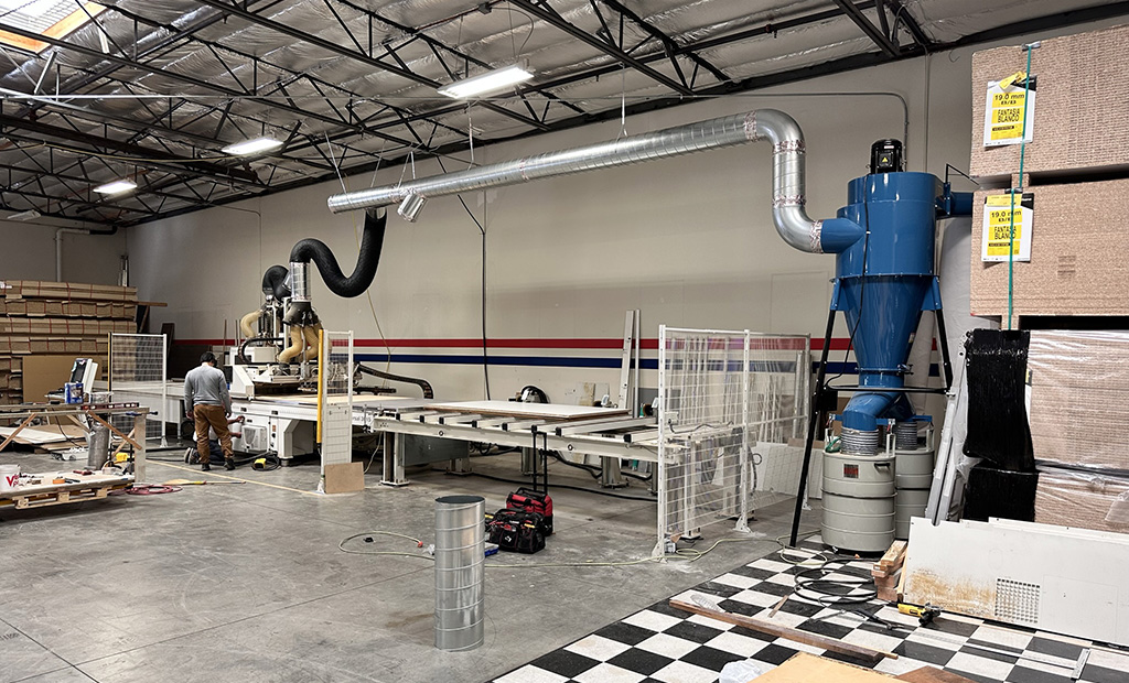 A large CNC industrial wood cutting machine along the wall of a warehouse, stacks of materials are on either side almost to the ceiling.