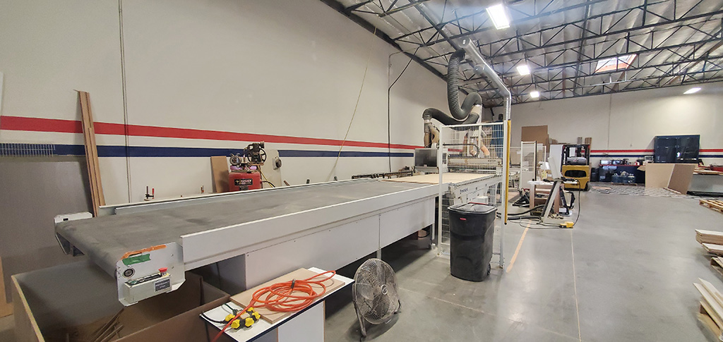 An automated CNC industrial wood cutting machine with the exit conveyor belt facing the camera.