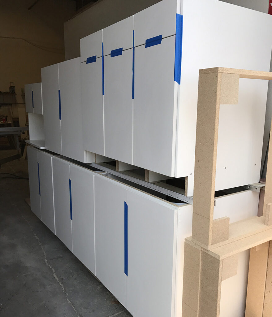 Two rows of white commercial cabinets cut in bulk by an automated CNC cutting machine.