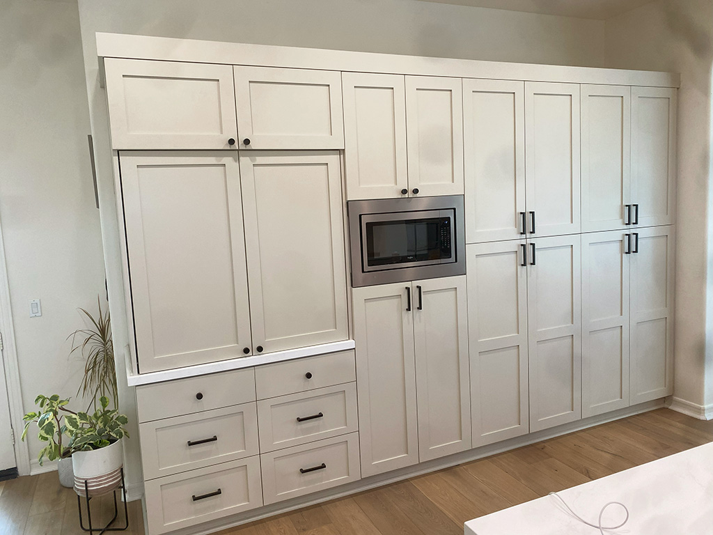 Custom built pantry along a whole wall, white drawers and cabinets, cutout for a microwave in the middle.