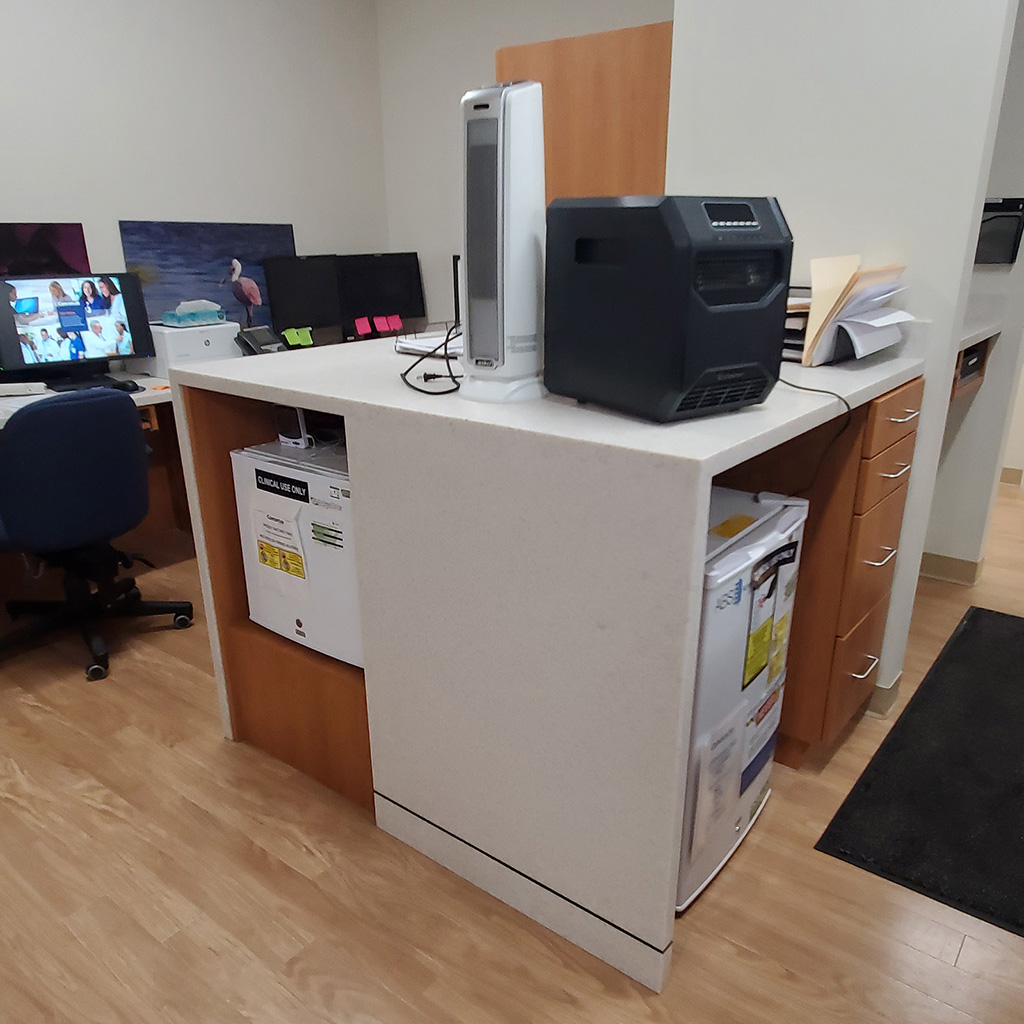 Custom built square office desk with cutouts for equipment and mini fridge.