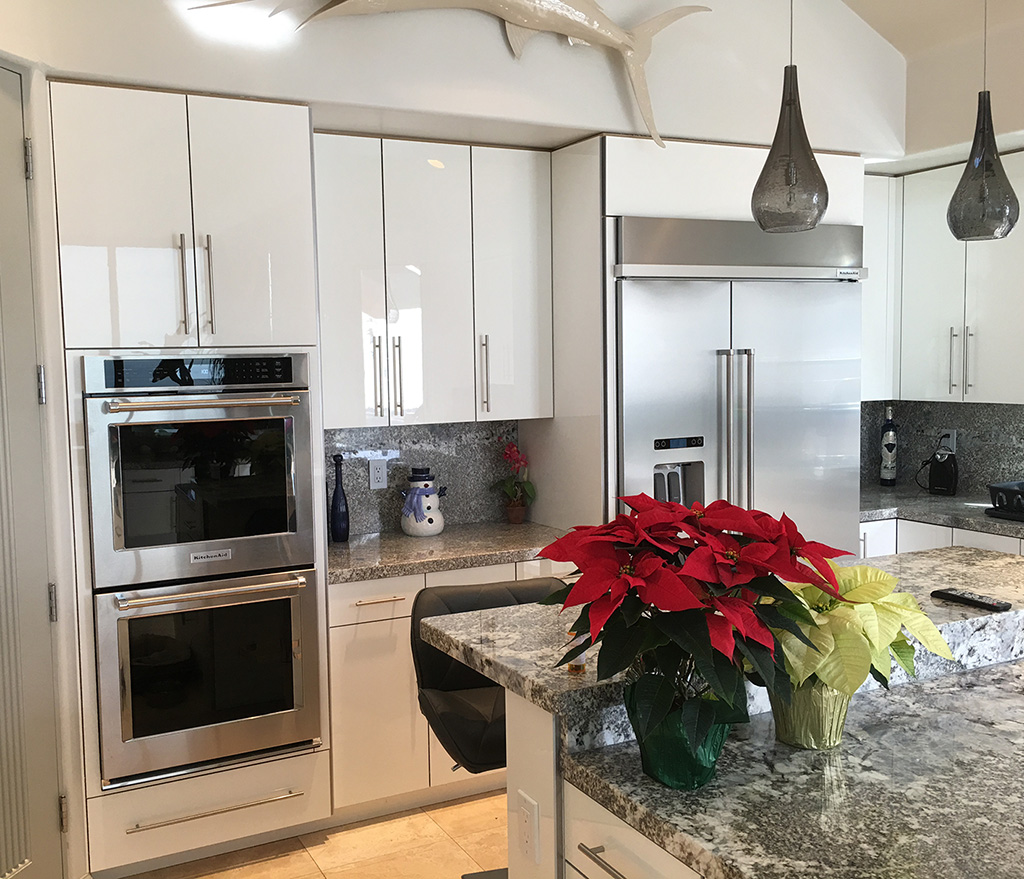 Interior kitchen remodel with white glossy cabinets, facing a silver double stove and refrigerator.